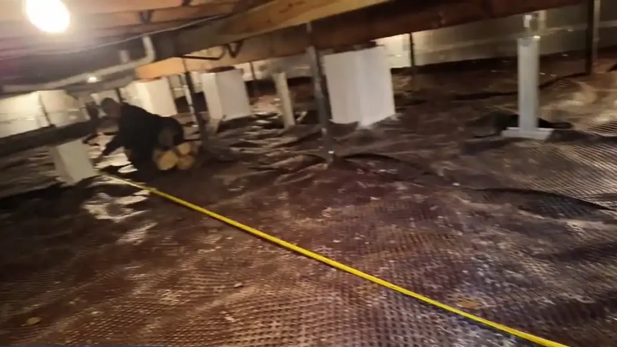 Tape measure stretched across a crawl space floor while a contractor measures the space