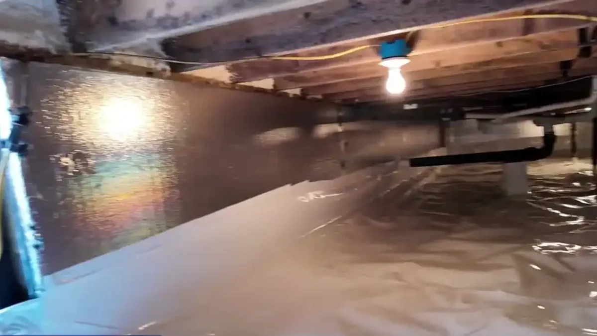Insulated crawl space wall and sealed white liner under a work light, an example of crawl space encapsulation in Raleigh, NC